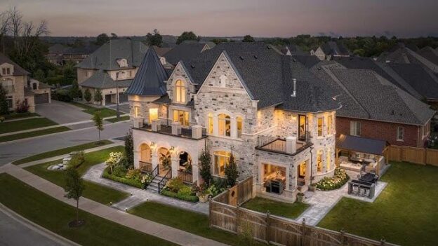 A luxurious stone-clad home in Nobleton, illuminated at dusk, featuring elegant architectural details and a beautifully landscaped yard.