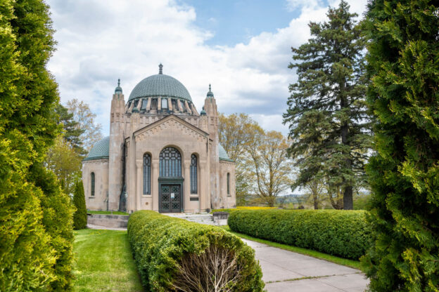 A historic domed building in Newmarket, surrounded by lush greenery and framed by neatly trimmed hedges and tall trees.