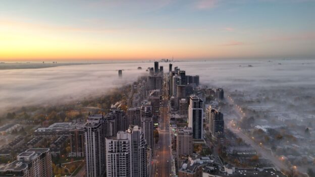 A breathtaking aerial view of North York at sunrise, with skyscrapers emerging through a blanket of fog and golden hues.