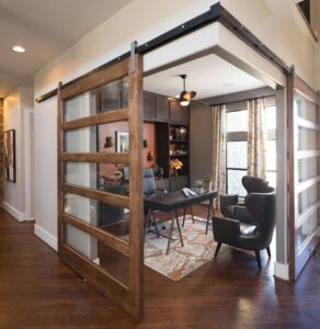 Modern home office with sliding glass-panel wooden barn doors, dark built-in shelving, and contemporary furniture accents.