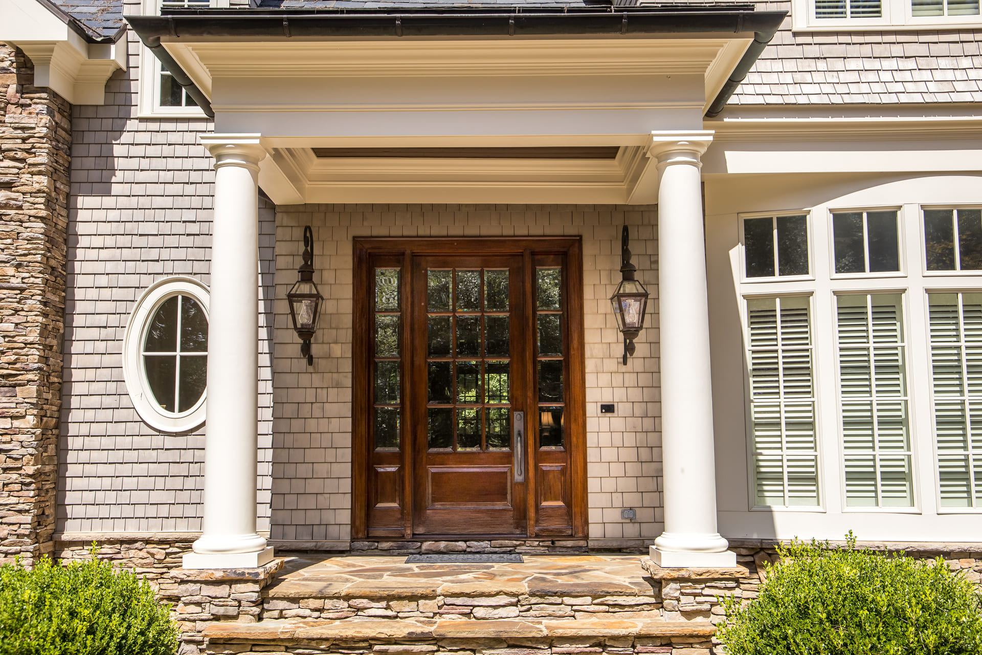 Custom solid wood entry door with glass panels, flanked by classic white columns and stone detailing, showcasing timeless craftsmanship on a traditional-style home exterior.