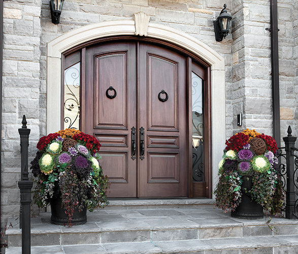 Custom arched wood double front entry door with decorative iron details and stone exterior.